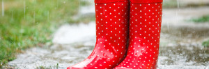 Das Bild zeigt rote Gummistiefel mit weissen Punkten in einer Wasserlacke stehend.